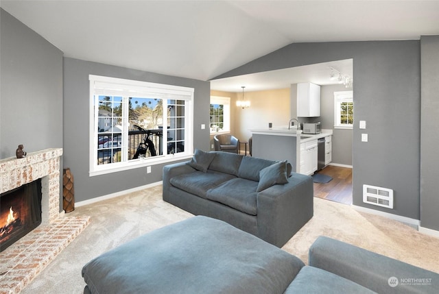 carpeted living room featuring lofted ceiling, sink, a notable chandelier, and a fireplace