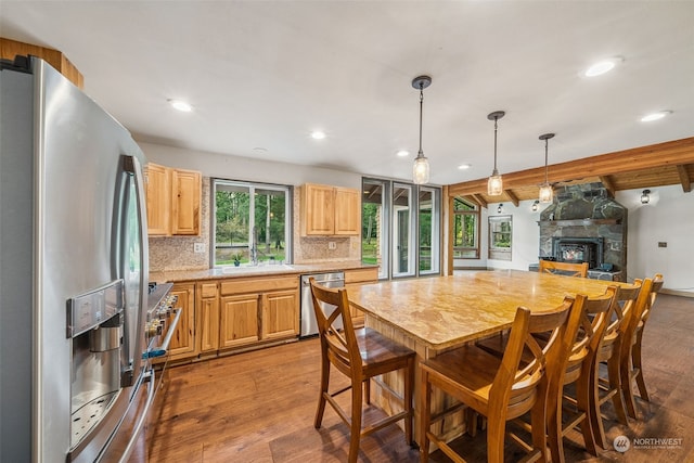 kitchen featuring appliances with stainless steel finishes, a fireplace, decorative backsplash, hardwood / wood-style flooring, and beam ceiling