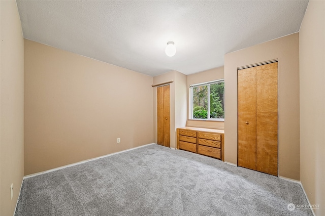 unfurnished bedroom with multiple closets, carpet floors, and a textured ceiling