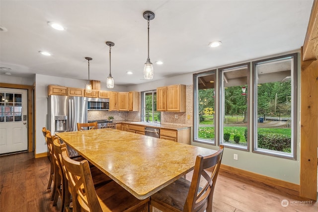 kitchen featuring pendant lighting, appliances with stainless steel finishes, light hardwood / wood-style floors, and tasteful backsplash