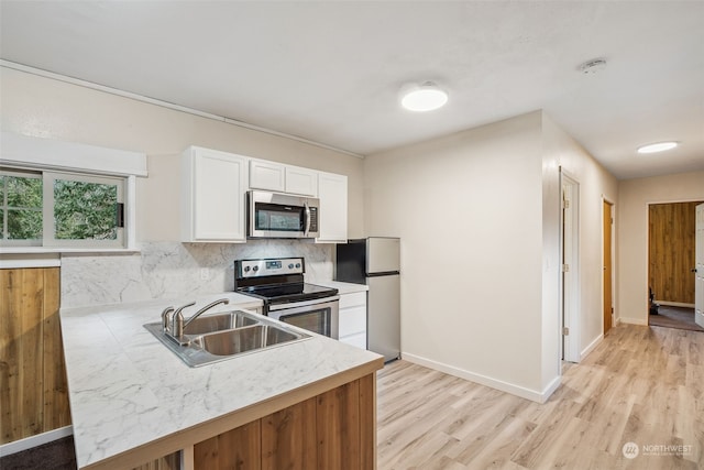 kitchen with sink, light hardwood / wood-style flooring, appliances with stainless steel finishes, white cabinets, and decorative backsplash