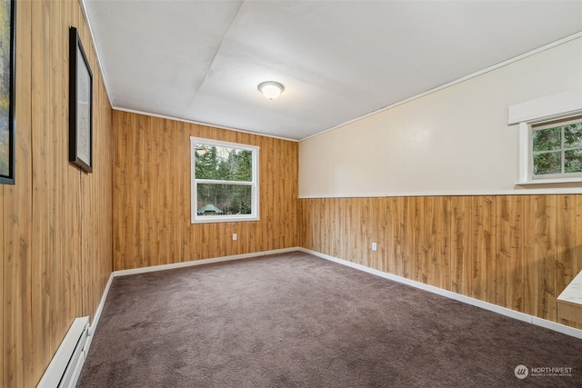 carpeted empty room with wood walls and a baseboard heating unit