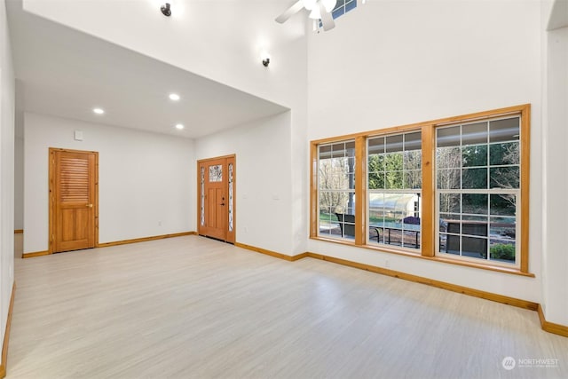 interior space with a towering ceiling, ceiling fan, and light wood-type flooring