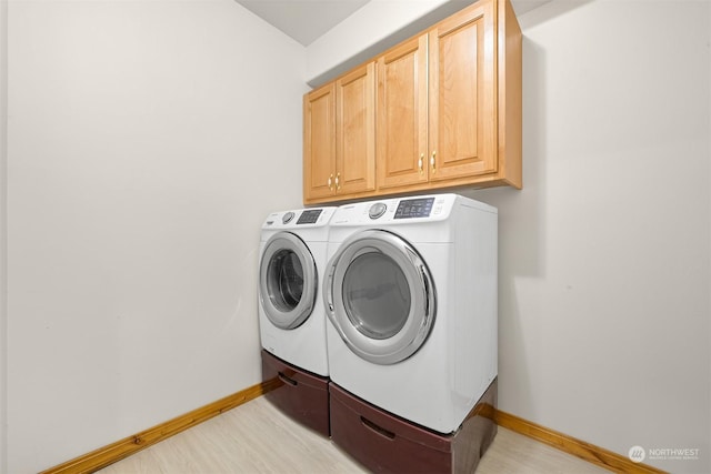 clothes washing area with cabinets, washer and dryer, and light hardwood / wood-style flooring