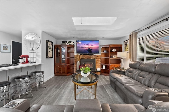 living room featuring wood-type flooring, a brick fireplace, and a skylight