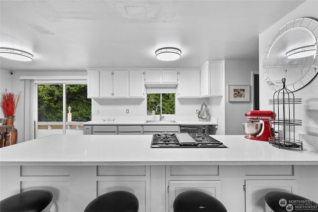 kitchen with stainless steel gas stovetop, white cabinetry, sink, and a kitchen bar