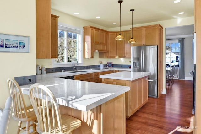 kitchen with sink, a breakfast bar area, hanging light fixtures, a center island, and stainless steel fridge with ice dispenser