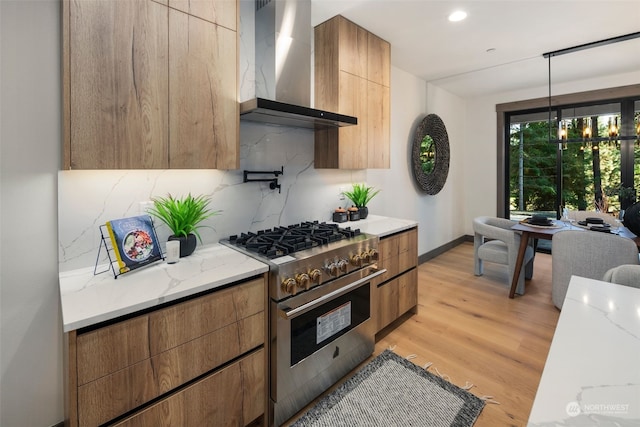 kitchen featuring high end stainless steel range oven, hanging light fixtures, decorative backsplash, wall chimney exhaust hood, and light wood-type flooring