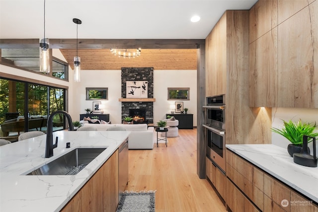 kitchen with pendant lighting, sink, double oven, a fireplace, and light stone countertops