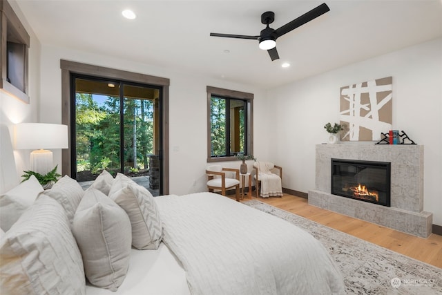 bedroom with a tiled fireplace, hardwood / wood-style flooring, access to exterior, and ceiling fan