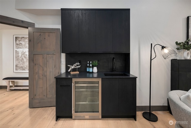 bar featuring sink, backsplash, light hardwood / wood-style floors, and beverage cooler