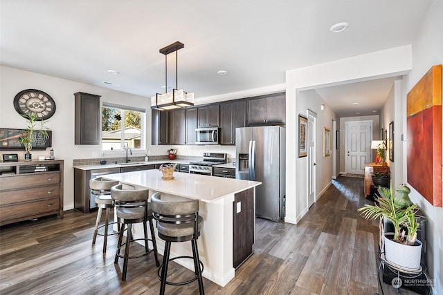 kitchen with stainless steel appliances, a center island, a kitchen breakfast bar, dark hardwood / wood-style flooring, and decorative light fixtures