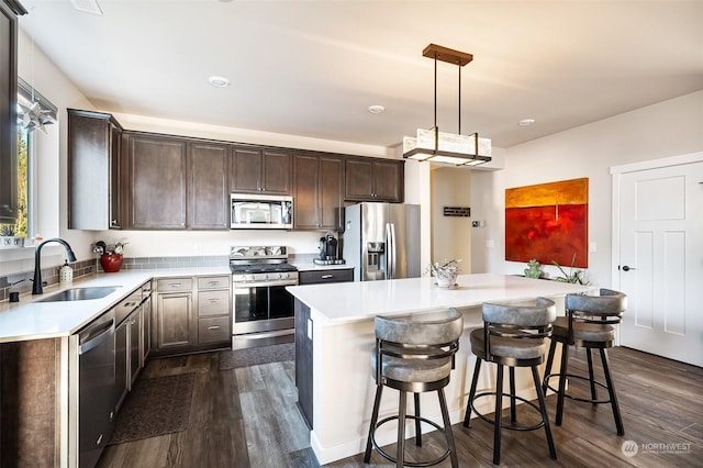 kitchen with dark wood-type flooring, sink, hanging light fixtures, a kitchen island, and stainless steel appliances