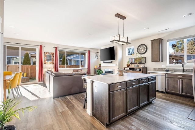 kitchen with pendant lighting, sink, a center island, stainless steel dishwasher, and dark brown cabinetry