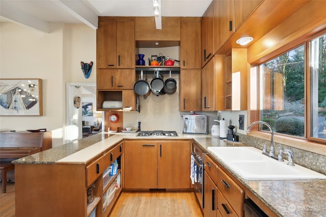 kitchen featuring sink, stainless steel gas cooktop, kitchen peninsula, light stone countertops, and light wood-type flooring