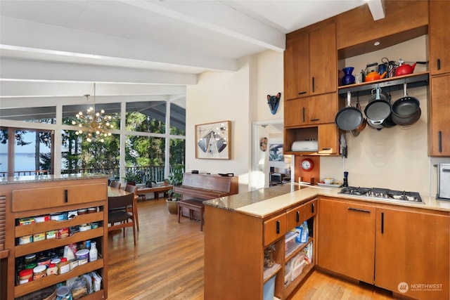 kitchen with light hardwood / wood-style flooring, vaulted ceiling with beams, stainless steel gas cooktop, kitchen peninsula, and a chandelier