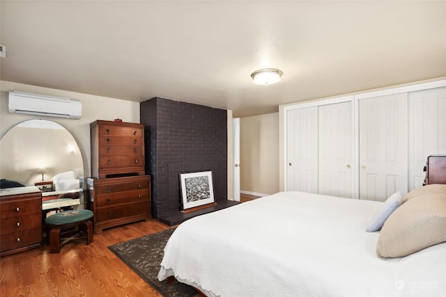 bedroom featuring hardwood / wood-style flooring, two closets, a fireplace, and a wall unit AC