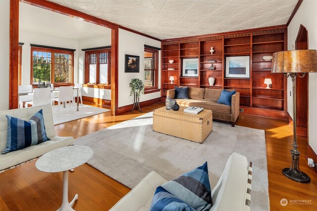 living room with built in features, light hardwood / wood-style flooring, and ornamental molding