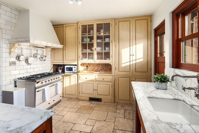 kitchen featuring sink, custom exhaust hood, light brown cabinets, high end stainless steel range oven, and decorative backsplash