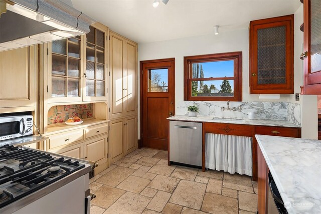 kitchen featuring range hood, tasteful backsplash, sink, stainless steel appliances, and cream cabinetry