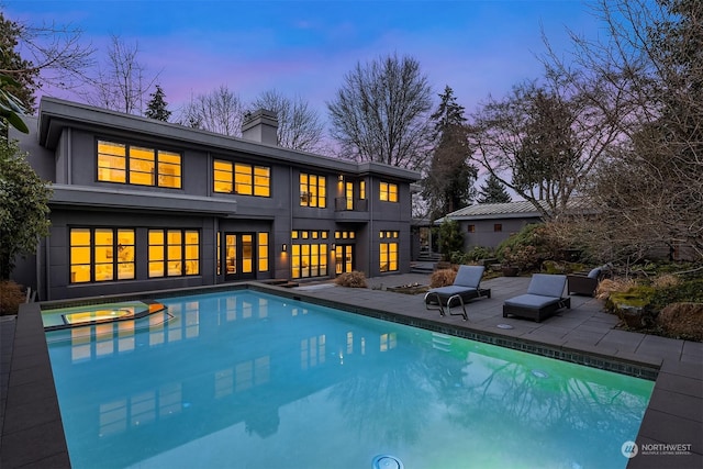 back house at dusk featuring a patio and a pool with hot tub