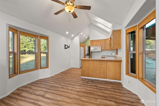 kitchen featuring sink, white appliances, hardwood / wood-style flooring, vaulted ceiling with skylight, and kitchen peninsula