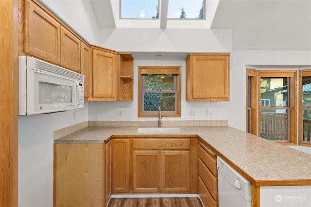 kitchen with white appliances, kitchen peninsula, sink, and a skylight