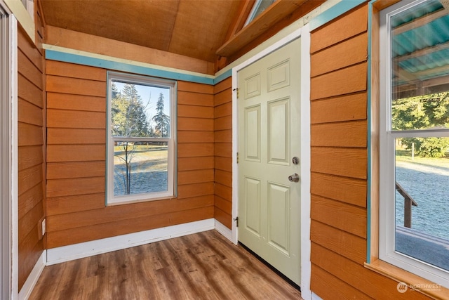 doorway with lofted ceiling, wooden walls, and hardwood / wood-style floors