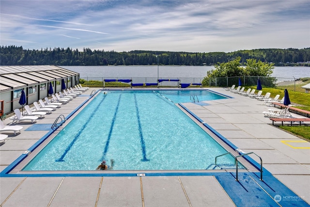 community pool featuring a patio area, fence, a forest view, and a water view