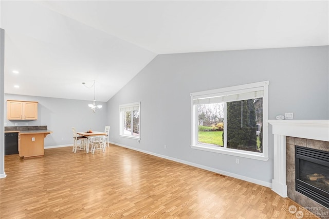 unfurnished living room featuring a tiled fireplace, a wealth of natural light, lofted ceiling, and light wood-type flooring