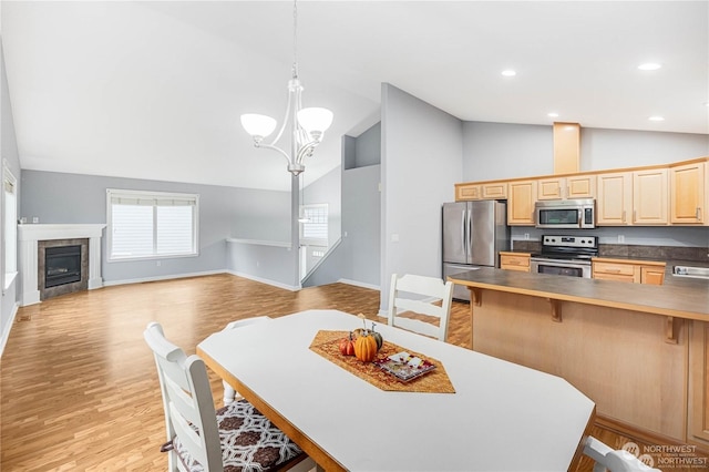 kitchen with appliances with stainless steel finishes, a fireplace, decorative light fixtures, lofted ceiling, and a chandelier