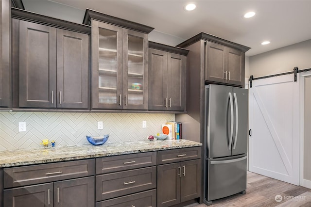 kitchen featuring light hardwood / wood-style flooring, a barn door, stainless steel refrigerator, dark brown cabinets, and decorative backsplash