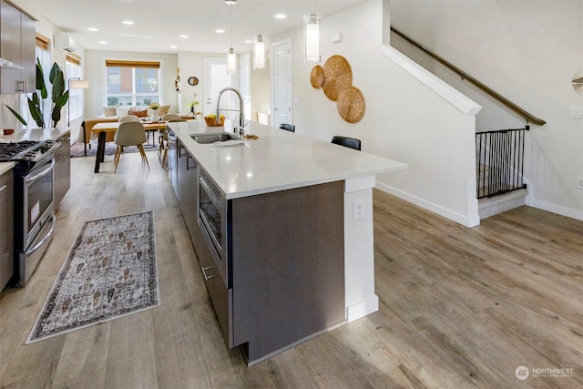 kitchen with dark brown cabinetry, sink, hanging light fixtures, an island with sink, and stainless steel appliances