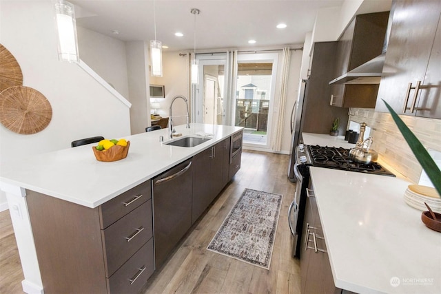 kitchen featuring decorative light fixtures, sink, a kitchen island with sink, stainless steel appliances, and light hardwood / wood-style flooring