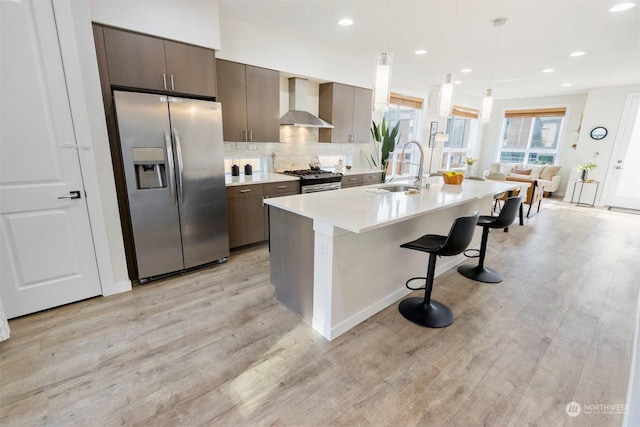 kitchen with pendant lighting, sink, a breakfast bar area, appliances with stainless steel finishes, and wall chimney exhaust hood