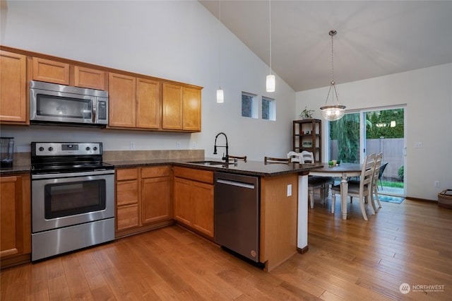 kitchen featuring pendant lighting, sink, light hardwood / wood-style floors, kitchen peninsula, and stainless steel appliances