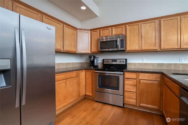 kitchen with appliances with stainless steel finishes, light hardwood / wood-style flooring, and dark stone counters