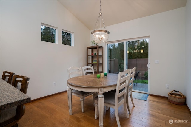 dining area with hardwood / wood-style flooring, a chandelier, and high vaulted ceiling