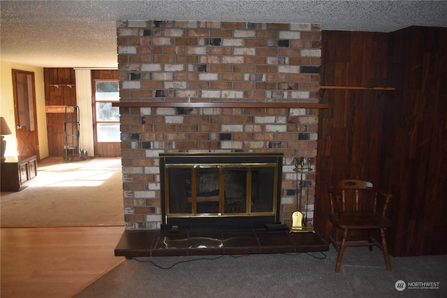 room details with wooden walls, carpet floors, a brick fireplace, and a textured ceiling