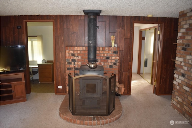 carpeted living room featuring a wood stove, a textured ceiling, and wooden walls