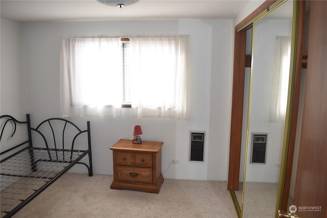 bedroom with light carpet, heating unit, and a closet