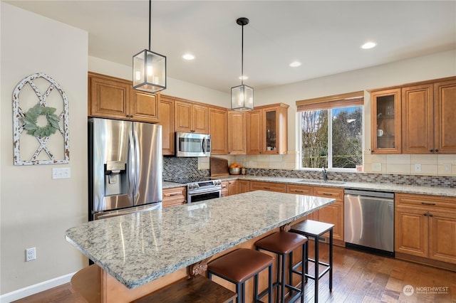 kitchen featuring a kitchen bar, dark hardwood / wood-style flooring, a kitchen island, stainless steel appliances, and light stone countertops