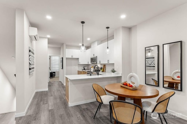 kitchen featuring light hardwood / wood-style flooring, stainless steel appliances, kitchen peninsula, white cabinets, and an AC wall unit