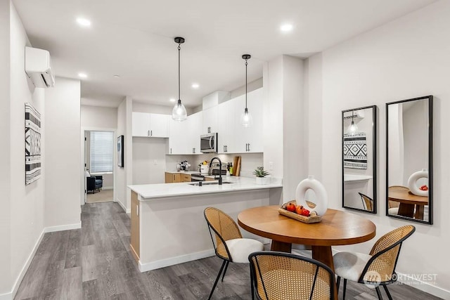 kitchen with wood-type flooring, a wall mounted air conditioner, appliances with stainless steel finishes, kitchen peninsula, and white cabinets