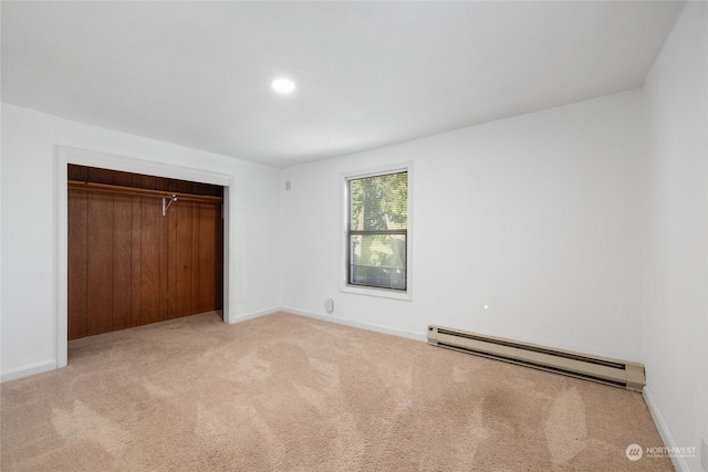 unfurnished bedroom featuring baseboard heating, light colored carpet, and a closet