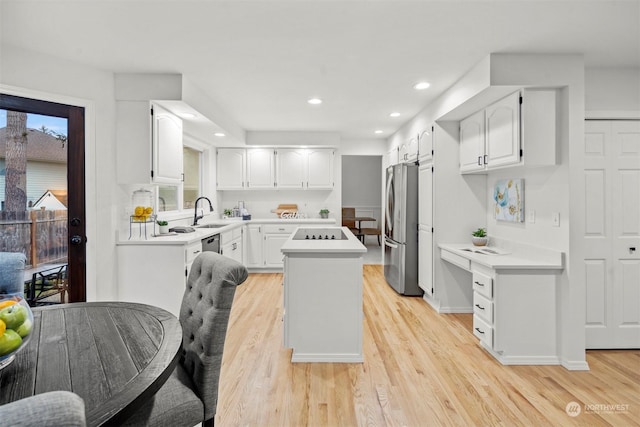 kitchen with a kitchen island, stainless steel refrigerator, sink, white cabinets, and light wood-type flooring