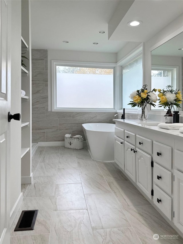 bathroom with vanity, a tub to relax in, and tile walls