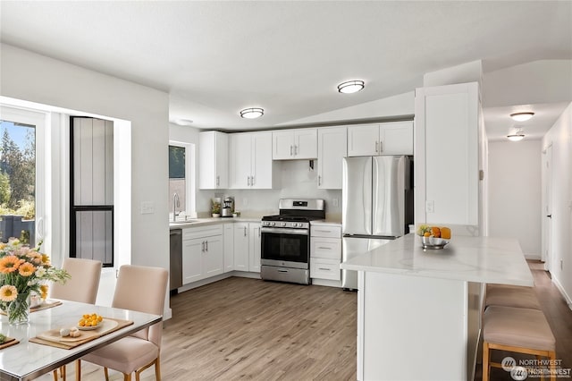 kitchen with sink, light hardwood / wood-style flooring, white cabinetry, stainless steel appliances, and a kitchen breakfast bar