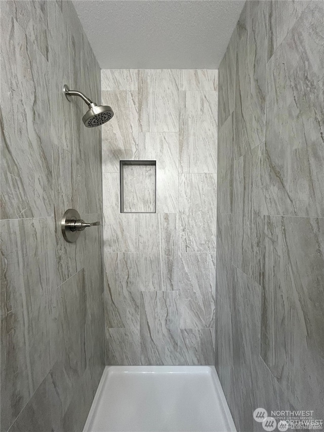 bathroom with a tile shower and a textured ceiling