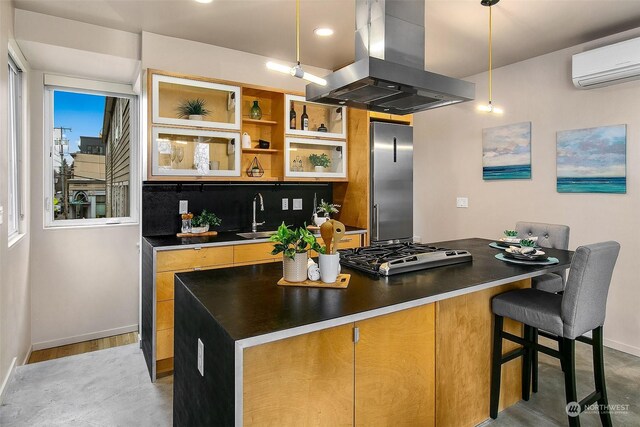 kitchen with appliances with stainless steel finishes, an AC wall unit, pendant lighting, sink, and island exhaust hood